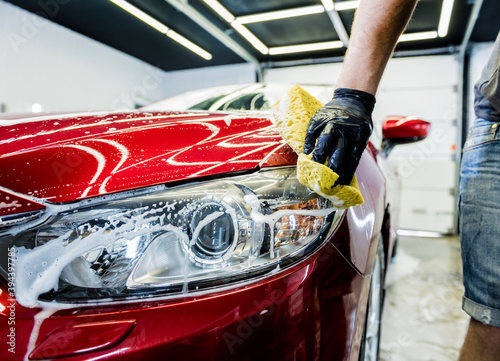 Worker washing red car with sponge on a car wash © romaset