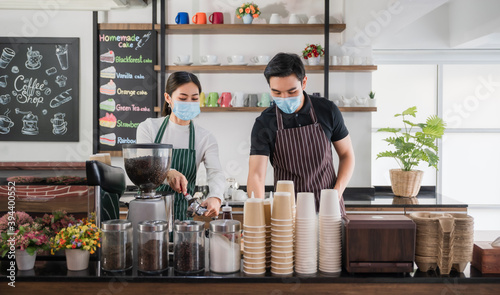 New normal startup small business of coffee shop concept. Male and female barista in face mask and standing behind bar counter in cafe.