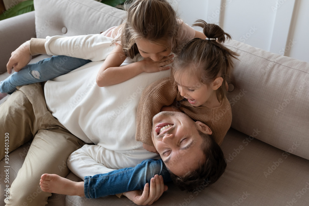 Funny father pretends to be tired or asleep while two pretty daughters want to play. Happy family lying on couch at home enjoy playtime active weekends together, having fun, games with kids concept Funny father pretends to be tired or asleep while two pretty daughters want to play. Happy family lying on couch at home enjoy playtime active weekends together, having fun, games with kids concept