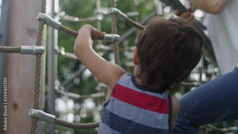 Son and his mom climbing a jungle gym in a playground on a sunny summer day Son and his mom climbing a jungle gym in a playground on a sunny summer day