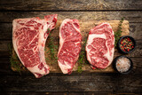 Variety of Fresh Raw Black Angus Prime Meat Steaks T-bone, New York, Ribeye and seasoning on wooden background, top view