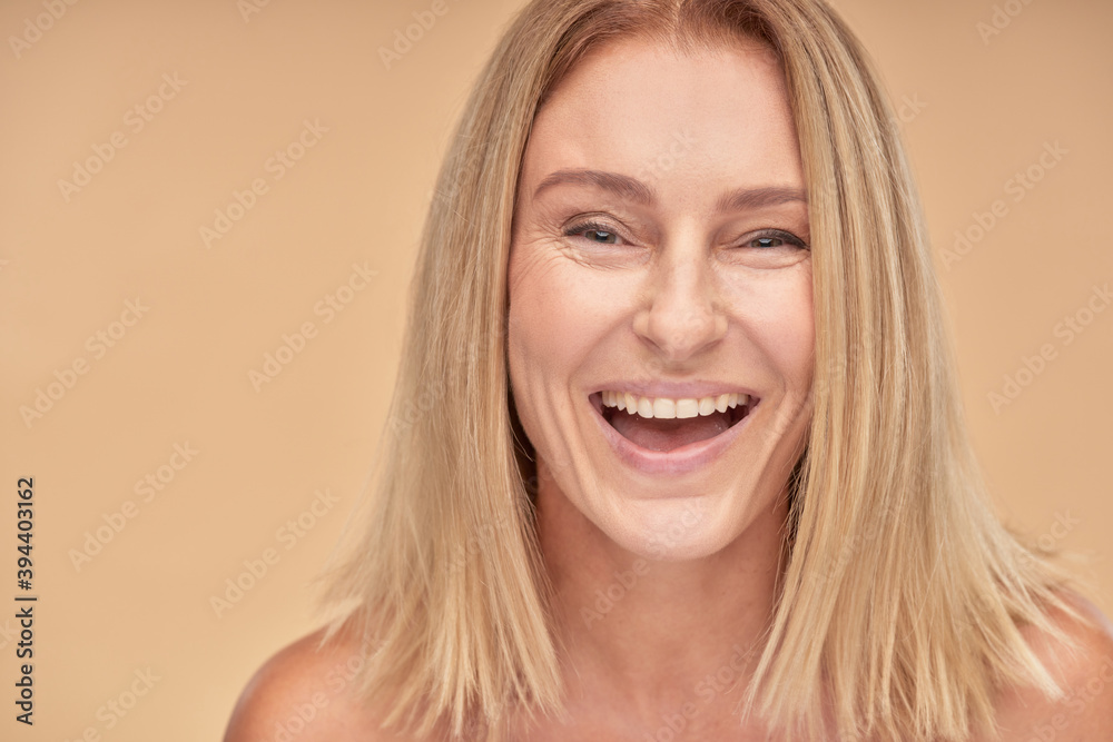 Fototapeta premium Portrait of attractive happy mature lady smiling at camera while posing over beige background in studio