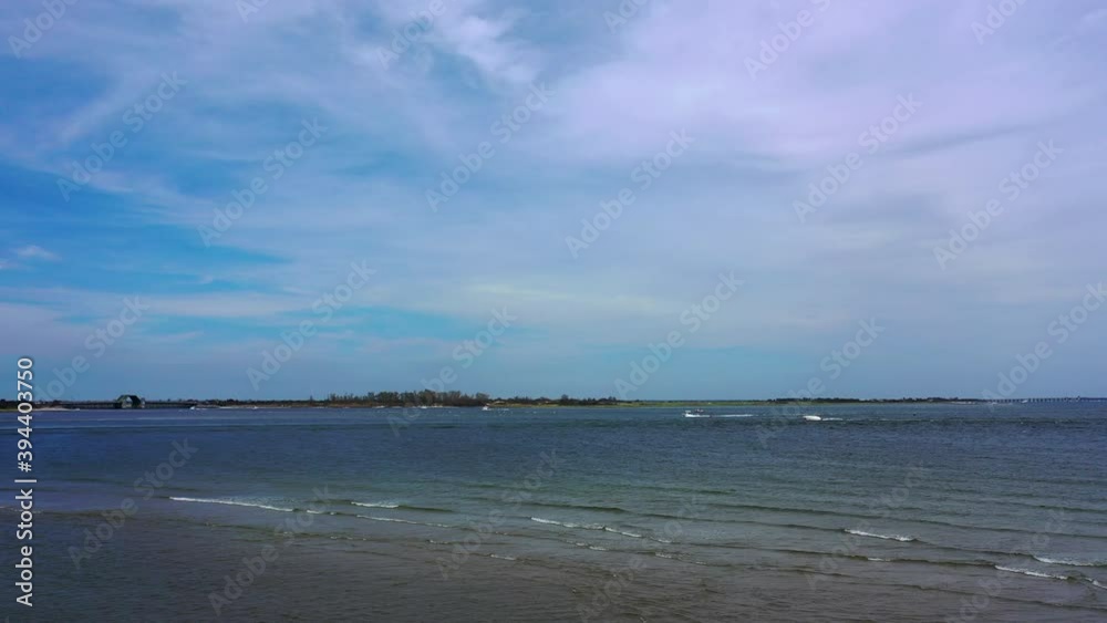 A low angle drone shot over a beach, looking out at the water & the horizon. It is at low tide on a sunny day. The camera is stationary as the waves go by below in this peaceful scene. A low angle drone shot over a beach, looking out at the water & the horizon. It is at low tide on a sunny day. The camera is stationary as the waves go by below in this peaceful scene.