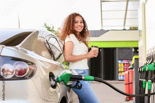 African-American woman drinking coffee while filling up car tank at gas station