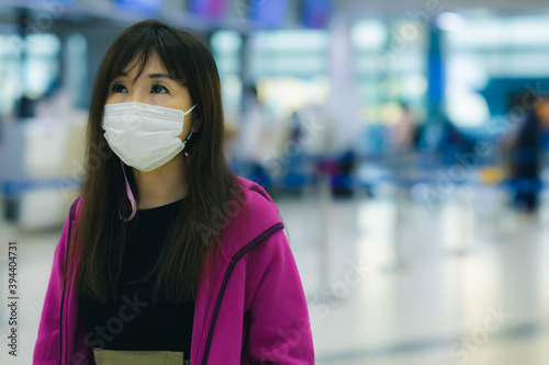 Traveler woman waiting at airport for domestic flight to some destination and looking timetable of airline for checking flight of airline at domestic airport. Pretty girl wear protective face mask 
