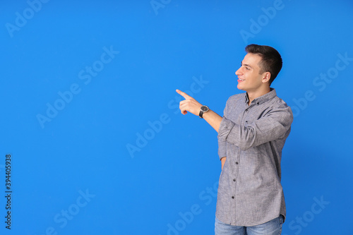 Young man with wristwatch showing something on color background