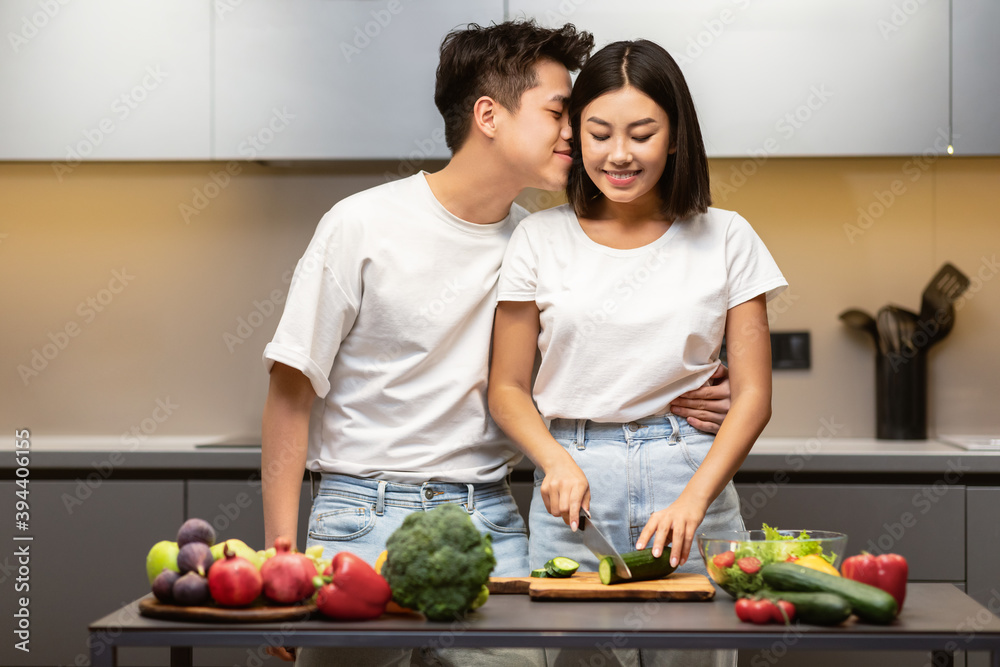 Loving Japanese Husband Kissing Wife Preparing Dinner Together In Kitchen Loving Japanese Husband Kissing Wife Preparing Dinner Together In Kitchen