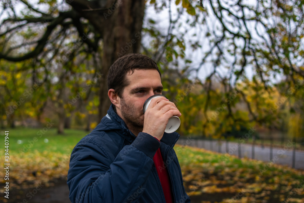 Photo of a young and attractive man enjoying a cup of coffee walking in the park during a day of autumn. Photo of a young and attractive man enjoying a cup of coffee walking in the park during a day of autumn.