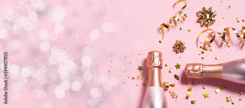 Fotografie, Obraz Long wide Christmas and New Year’s banner with rose Champagne bottles, golden decorations and bokeh lights on pink pastel background
