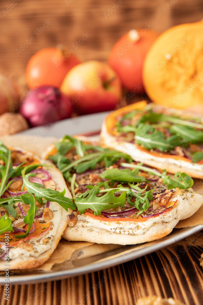 gebackener Flammkuchen mit Kürbis vom Hokkaido, Apfel, Zwiebelringen, Walnüssen, Frischkäse, Schmand, Rosmarin und Rucola auf einem Tisch aus Holz in der Küche gebackener Flammkuchen mit Kürbis vom Hokkaido, Apfel, Zwiebelringen, Walnüssen, Frischkäse, Schmand, Rosmarin und Rucola auf einem Tisch aus Holz in der Küche