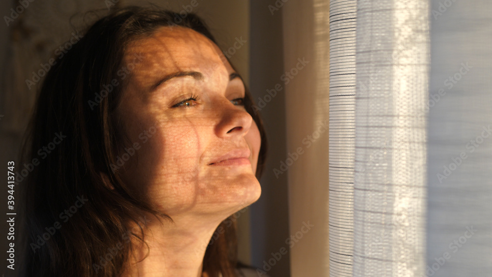 Young woman opening curtains looking through the window. Happy confident lady enjoying beautiful view and dreaming at home. Smiling girl contemplating feeling hope peaceful morning Young woman opening curtains looking through the window. Happy confident lady enjoying beautiful view and dreaming at home. Smiling girl contemplating feeling hope peaceful morning