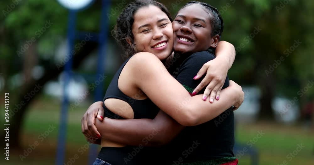 Diverse female friends hugging each other outside in park. Two girlfriends embrace