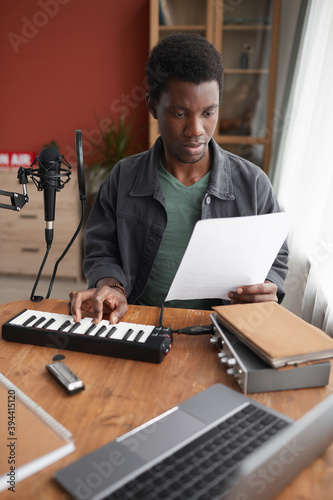 Vertical portrait of young African-American musician composing music in home recording studio