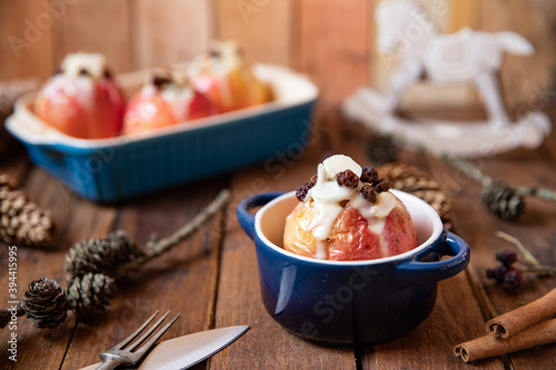 gebackener Bratapfel mit Füllung aus Marzipan, Mandeln, Rosinen und Zimt mit Vanillesoße zur Winterzeit und Weihnachten auf einem braunen Tisch aus Holz in der Küche