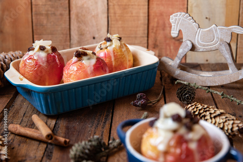 gebackener Bratapfel mit Füllung aus Marzipan, Mandeln, Rosinen und Zimt mit Vanillesoße zur Winterzeit und Weihnachten auf einem braunen Tisch aus Holz in der Küche