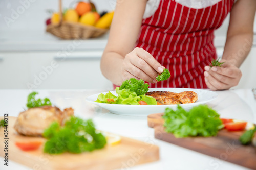 A beautiful Asian woman places parsley on a salmon steak arranged on a plate with green oak vegetables. Ideas about healthy cooking and weight loss. Soft focus
