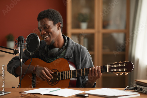 Fototapeta Portrait of talented African-American man singing to microphone and playing guit