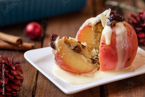 gebackener Bratapfel mit Füllung aus Marzipan, Mandeln, Rosinen und Zimt mit Vanillesoße zur Winterzeit und Weihnachten auf einem braunen Tisch aus Holz in der Küche