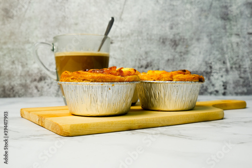 Selective focus picture of freshly baked egg tarts with milk coffee insight on wooden board.