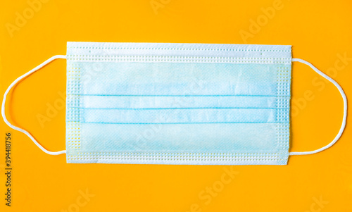 Disposable medical protective mask in blue with an ear loop to cover the mouth and nose to protect against bacteria on a bright orange background, close-up, top view. Concept of respiratory protection
