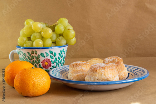 Front view of a still life with some traditional Spanish cakes, grapes and mandarins presented in traditional hand painted ceramic.