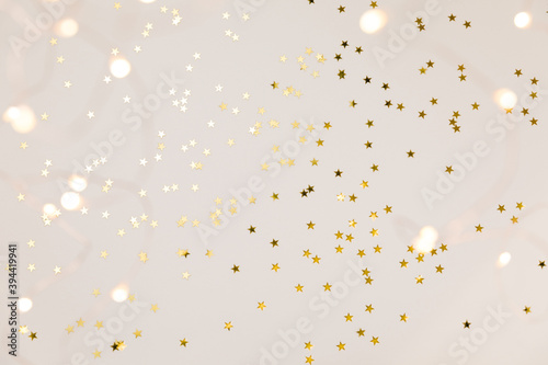 Festive gold background. Shining stars confetti and fairy lights on beige and Set Sail Champagne background. Christmas. Wedding. Birthday. Flat lay, top view, copy space