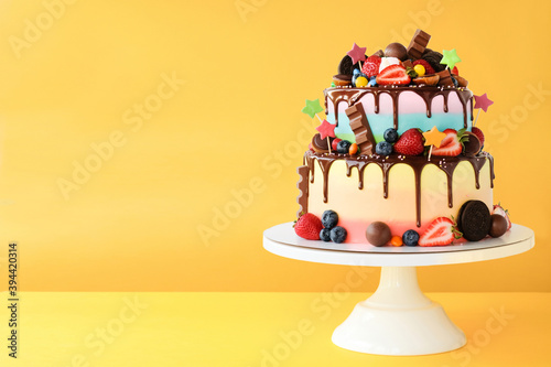 Photography Cake on birthday with colorful rainbow cream on a yellow background decorated with berries, colorful sprinkles, poured with chocolate