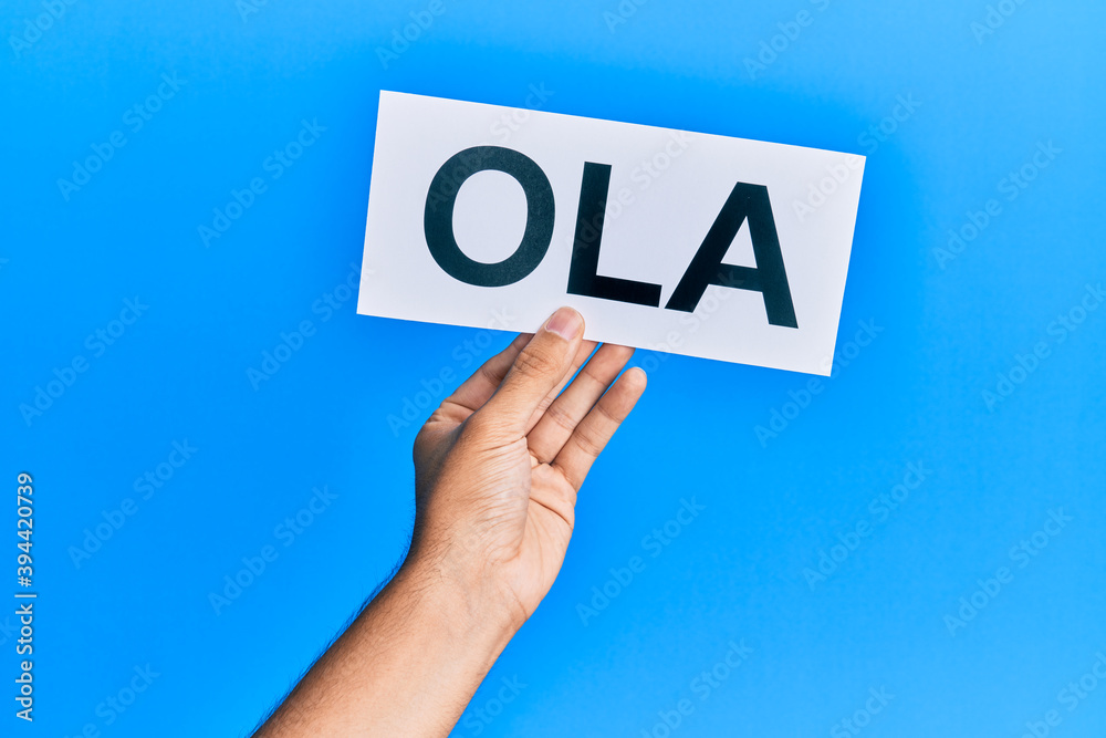 Hand of hispanic man holding ola word paper over isolated blue background. Hand of hispanic man holding ola word paper over isolated blue background.