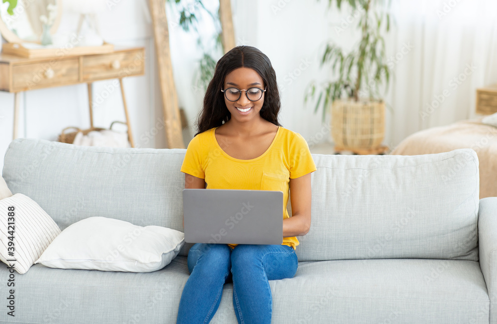 Cheerful black lady sitting on comfy couch with laptop and communicating to her friend at home Cheerful black lady sitting on comfy couch with laptop and communicating to her friend at home