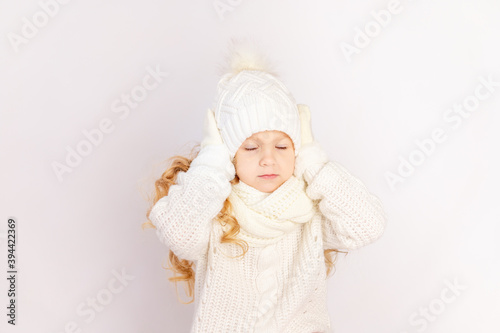 child girl in a sweater and hat holding her head with closed eyes on a white isolated background, space for text