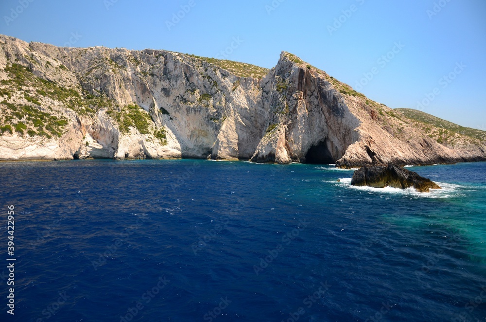 Limestone rocks on the coast of Zakynthos island, Greece. Sunny day, crystal clear water, blue sky, boat trip, rocks falling steeply into the sea.