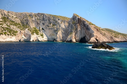 Limestone rocks on the coast of Zakynthos island, Greece. Sunny day, crystal clear water, blue sky, boat trip, rocks falling steeply into the sea.