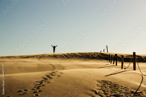 Krajobraz pustynny błękitne niebo i ruchome piaski z sylwetką idącego człowieka w pięknym świetle zachodzącego słońca	
