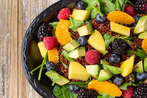 A top down view of a tropical salad, featuring spinach, fruit and quinoa.
