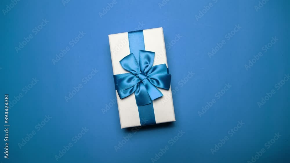Stop motion photography concept. Close-up of Christmas white gift box with blue bow, on background of blue color.