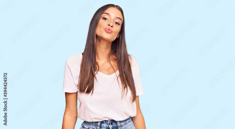 Young hispanic woman wearing casual white tshirt looking at the camera blowing a kiss on air being lovely and sexy. love expression. Young hispanic woman wearing casual white tshirt looking at the camera blowing a kiss on air being lovely and sexy. love expression.