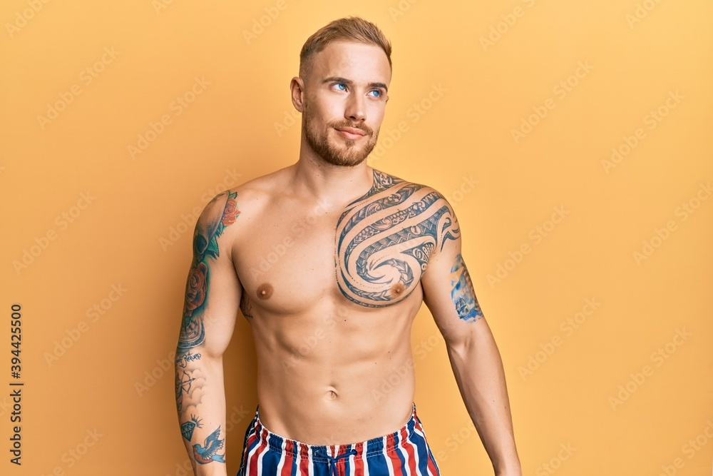 Fototapeta premium Young caucasian man wearing swimwear shirtless smiling looking to the side and staring away thinking.
