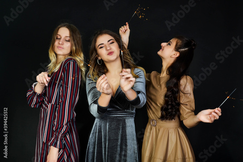 Adorable three cute teenage white girls posing with bengal lights om black background. Gorgeous women holding sparklers and laughing in new year.