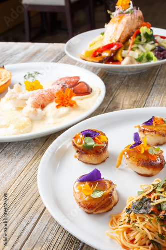 A view of several gourmet presented seafood dishes, featuring scallops, lobster tail and salmon.