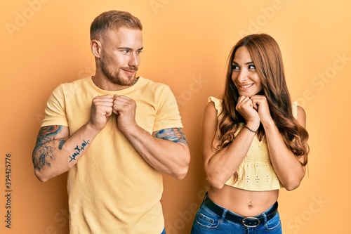 Young couple of girlfriend and boyfriend hugging and standing together laughing nervous and excited with hands on chin looking to the side