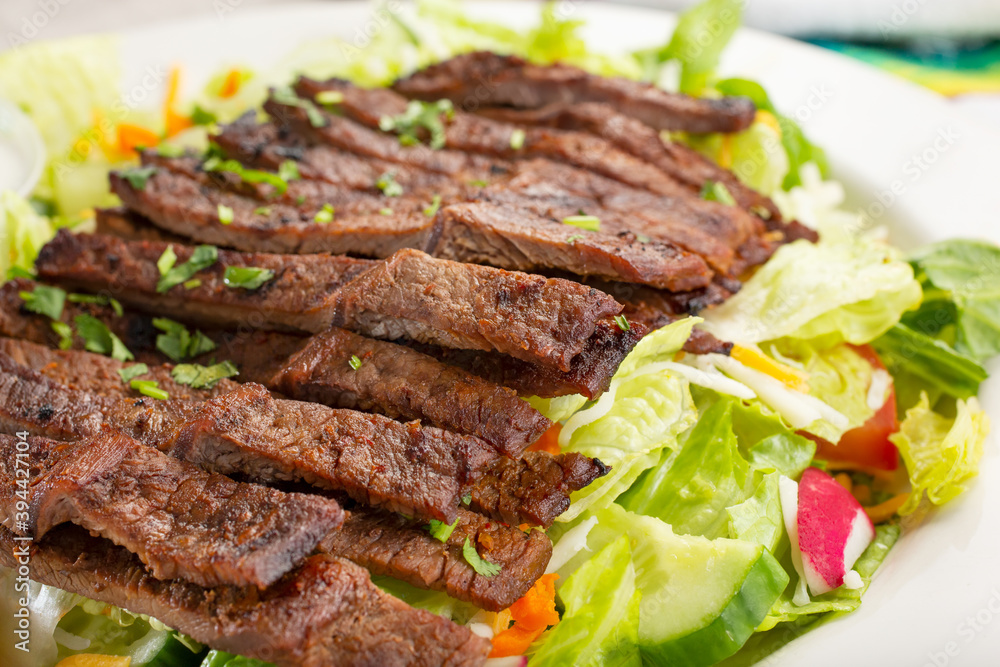 A view of a carne asada salad, in a restaurant or kitchen setting.