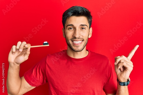 Young handsome man holding toothbrush with toothpaste smiling happy pointing with hand and finger to the side