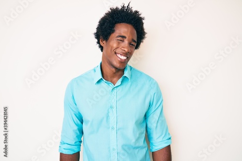 Handsome african american man with afro hair wearing casual clothes winking looking at the camera with sexy expression, cheerful and happy face.