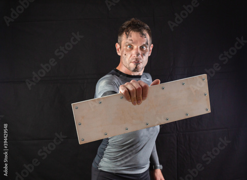 A sporty man holding an empty wooden sign with screws on a black background. Concept for inserting any word