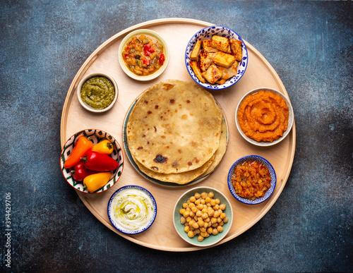 Indian Thali - selection of various dishes served on round wooden platter. Assorted Indian vegetarian meze with traditional chapati bread, paneer, dal, chutney in different bowls. Top view