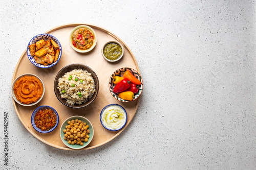 Indian Thali - selection of various dishes served on round wooden platter. Assorted Indian vegetarian meze with boiled basmati rice, paneer, dal, chutney in different bowls. Top view, space for text