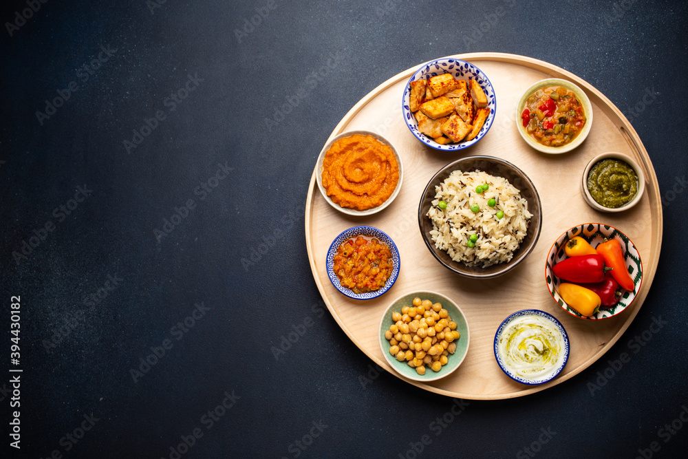 Indian Thali - selection of various dishes served on round wooden platter. Assorted Indian vegetarian meze with boiled basmati rice, paneer, dal, chutney in different bowls. Top view, space for text