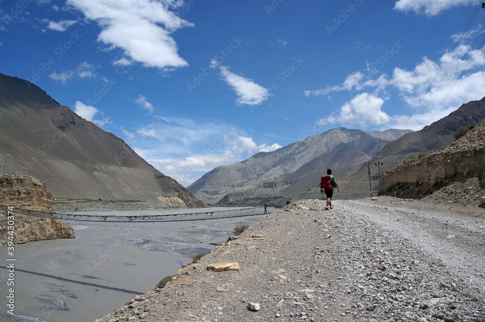 Tourist goes along the banks of the Kali Gandaki River, against the backdrop of the Himalayan mountains. Trekking to the Upper Mustang. Nepal.