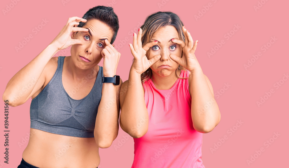 Couple of women wearing sportswear trying to open eyes with fingers, sleepy and tired for morning fatigue Couple of women wearing sportswear trying to open eyes with fingers, sleepy and tired for morning fatigue