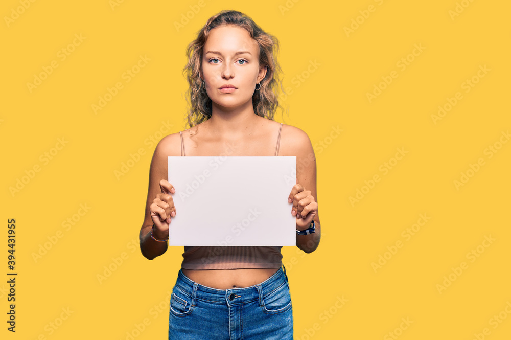 Beautiful caucasian woman holding blank empty banner thinking attitude and sober expression looking self confident Beautiful caucasian woman holding blank empty banner thinking attitude and sober expression looking self confident